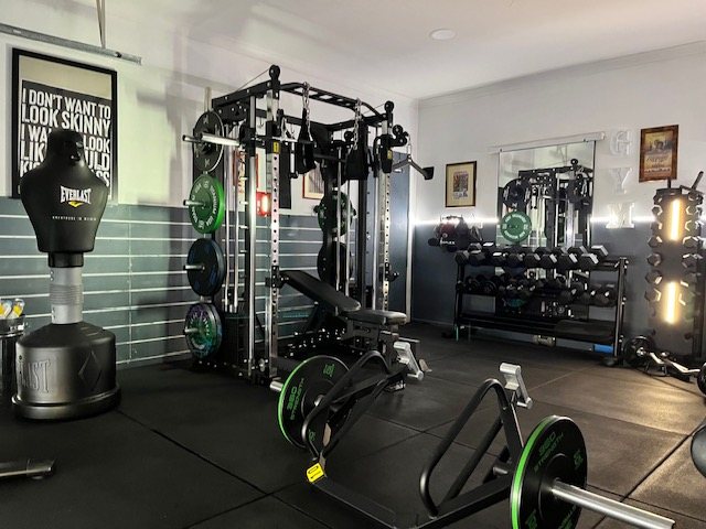 Kevin's private studio in Eynesbury: a power rack loaded with plates, a bench, a dumbbell rack, a landmine station and a boxing bag on rubber flooring